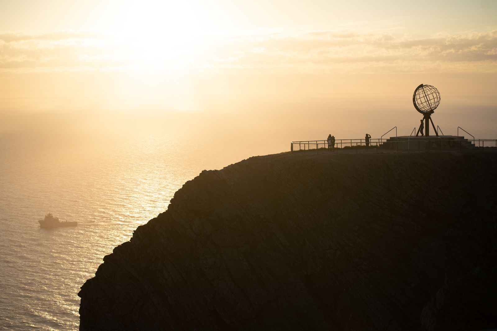Visitors on the North Cape cliff beside the globe monument, silhouetted against the low northern sun, a goal of North Cape cruises