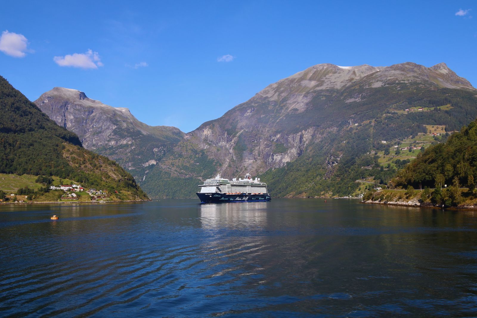 Cruise ship sailing a calm Norwegian fjord between steep mountains on a sunny Scandinavia cruise